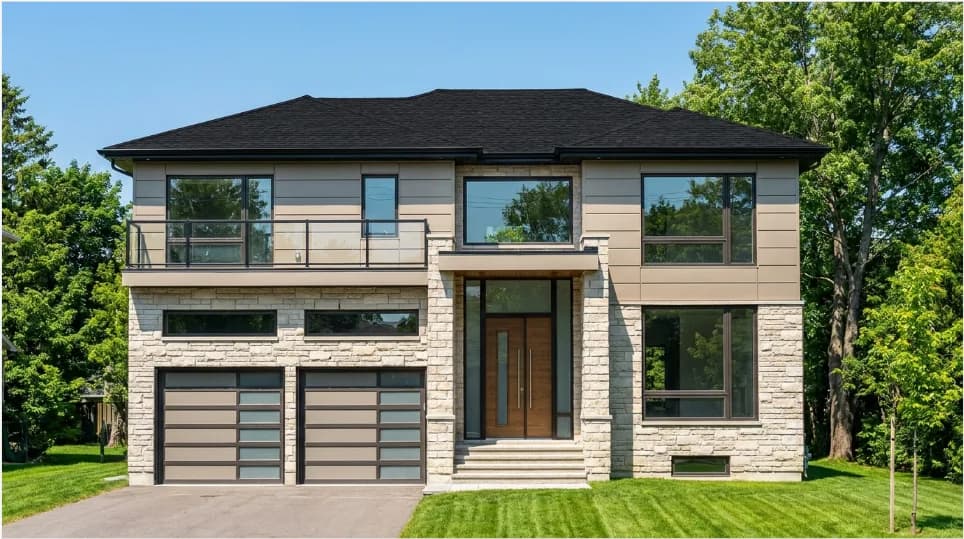 Supplied front exterior image of 1393 Selkirk with pale upper cladding, a balcony, stone ground-floor walls, two garage doors and a central entrance