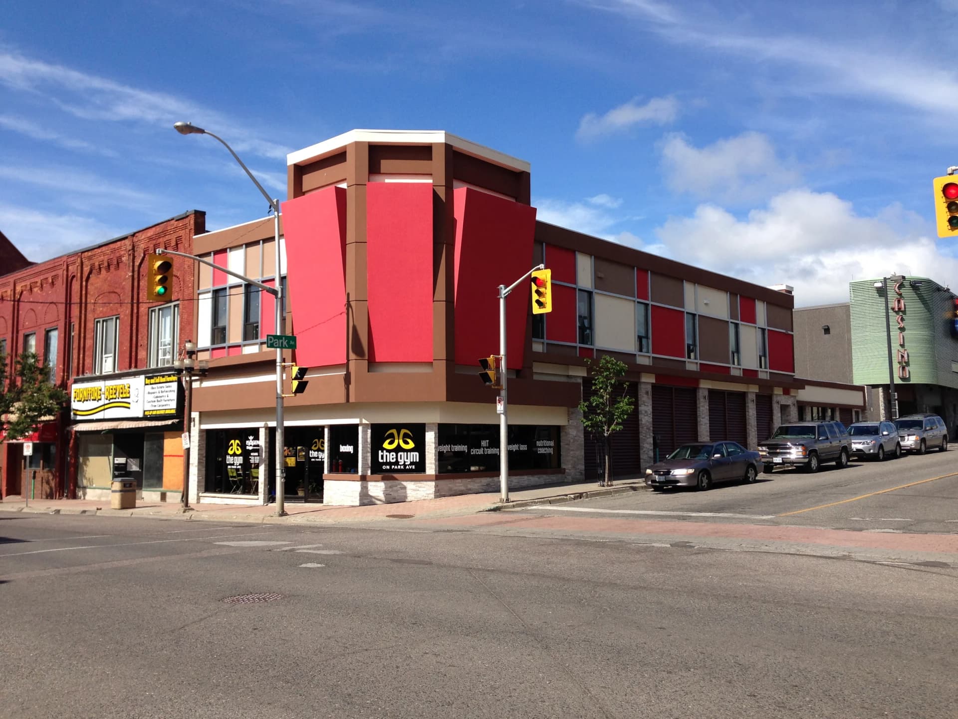 Wide photograph of 30 Cumberland Street South showing the red and grey upper facade, ground-floor corner storefront and neighbouring brick buildings