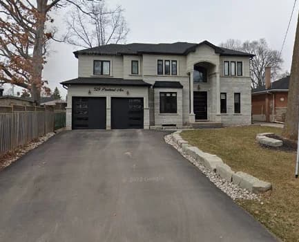 Daytime photograph of 526 Pineland showing pale stone walls, two dark garage doors, an arched entrance and a driveway beside the front lawn