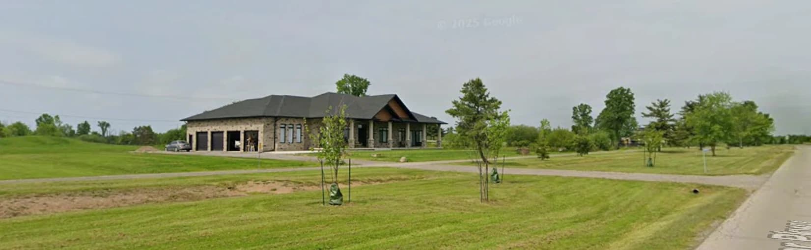 Wider supplied street view of 3405 Niagara River Parkway showing the stone garage wing, covered porch, driveway and surrounding lawn