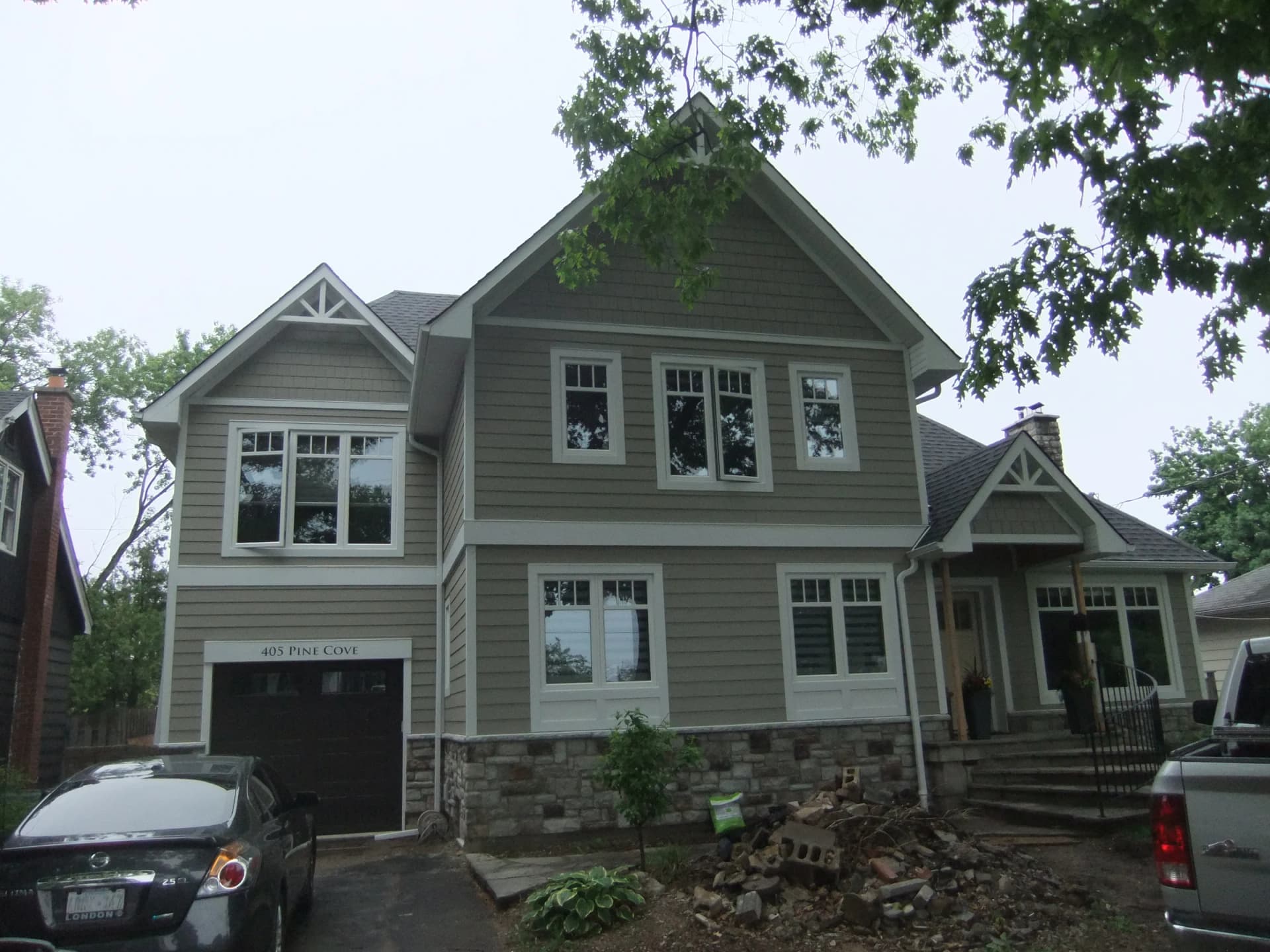 Exterior photograph of 405 Pine Cove with gabled roofs, siding, white-trimmed windows, a covered porch and construction materials in front of the house