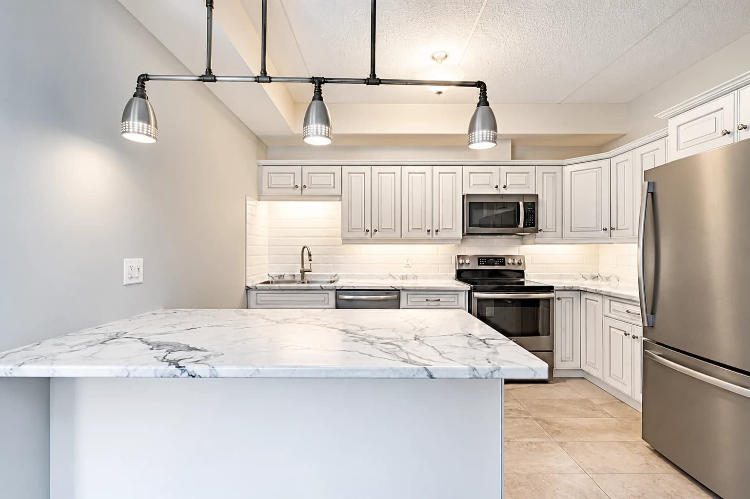 White suite kitchen with a marble-pattern peninsula, stainless-steel appliances and industrial pendant lighting