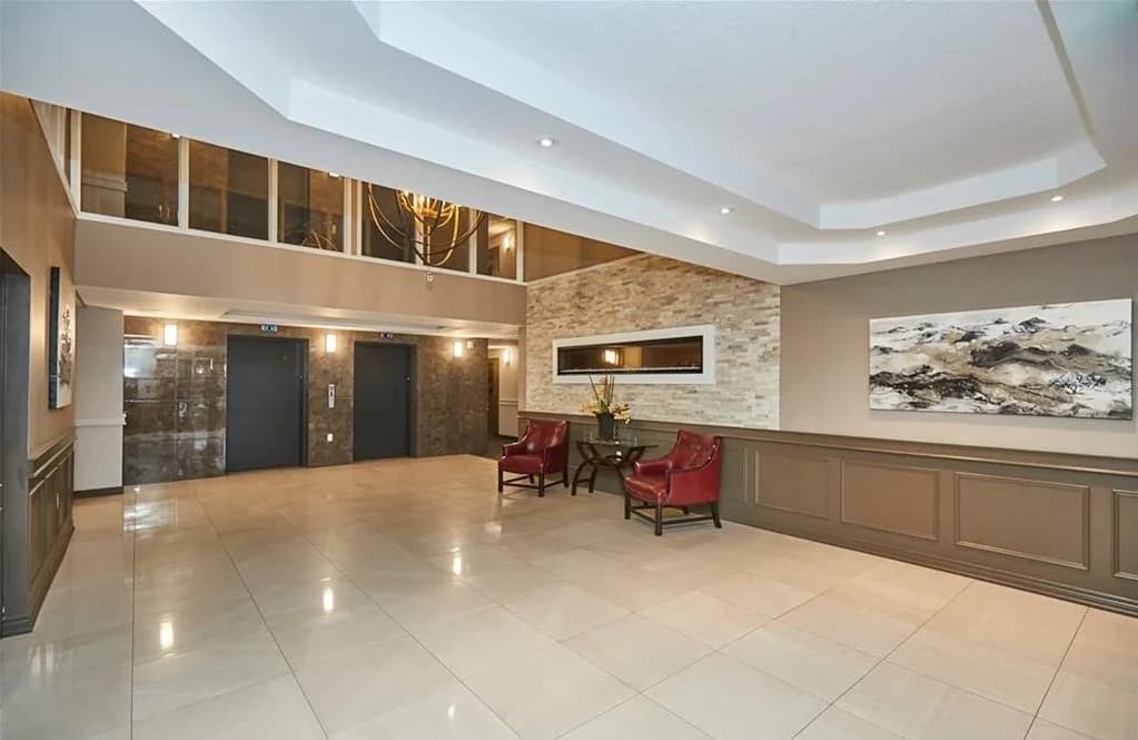 Olympia entrance lobby with two elevator doors, a stone accent wall, red armchairs and a glazed mezzanine