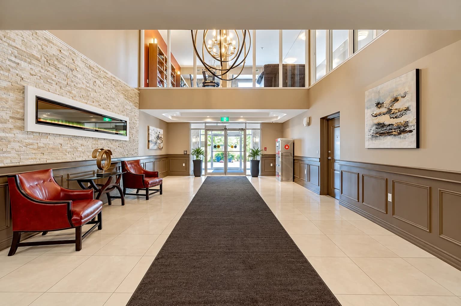 Double-height entrance lobby with a stone accent wall, leather chairs and a glazed mezzanine