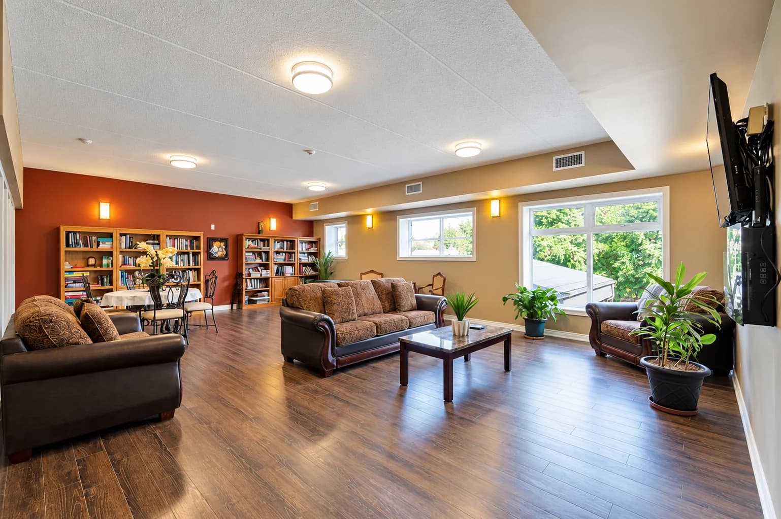 Residents' lounge with sofas, bookcases, dining tables and large windows overlooking greenery