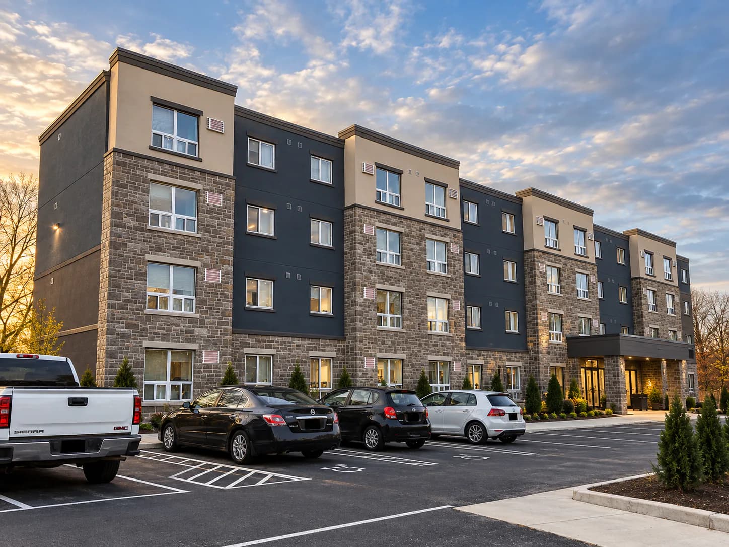 Parking-side exterior view of the four-storey apartment building at 574 King Street with stone walls, dark facade panels and rows of windows