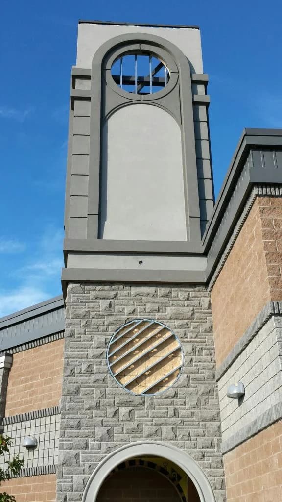Stone-clad church tower with circular openings and an arched entrance during construction