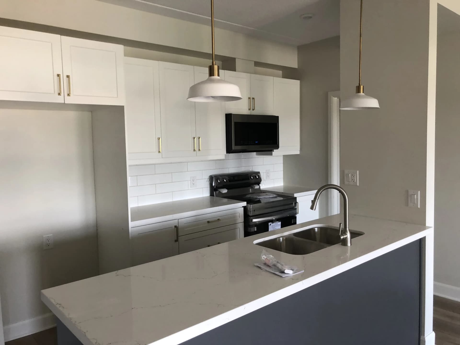 Apartment kitchen with white cabinets, dark appliances, pendant lights and an island with an inset sink