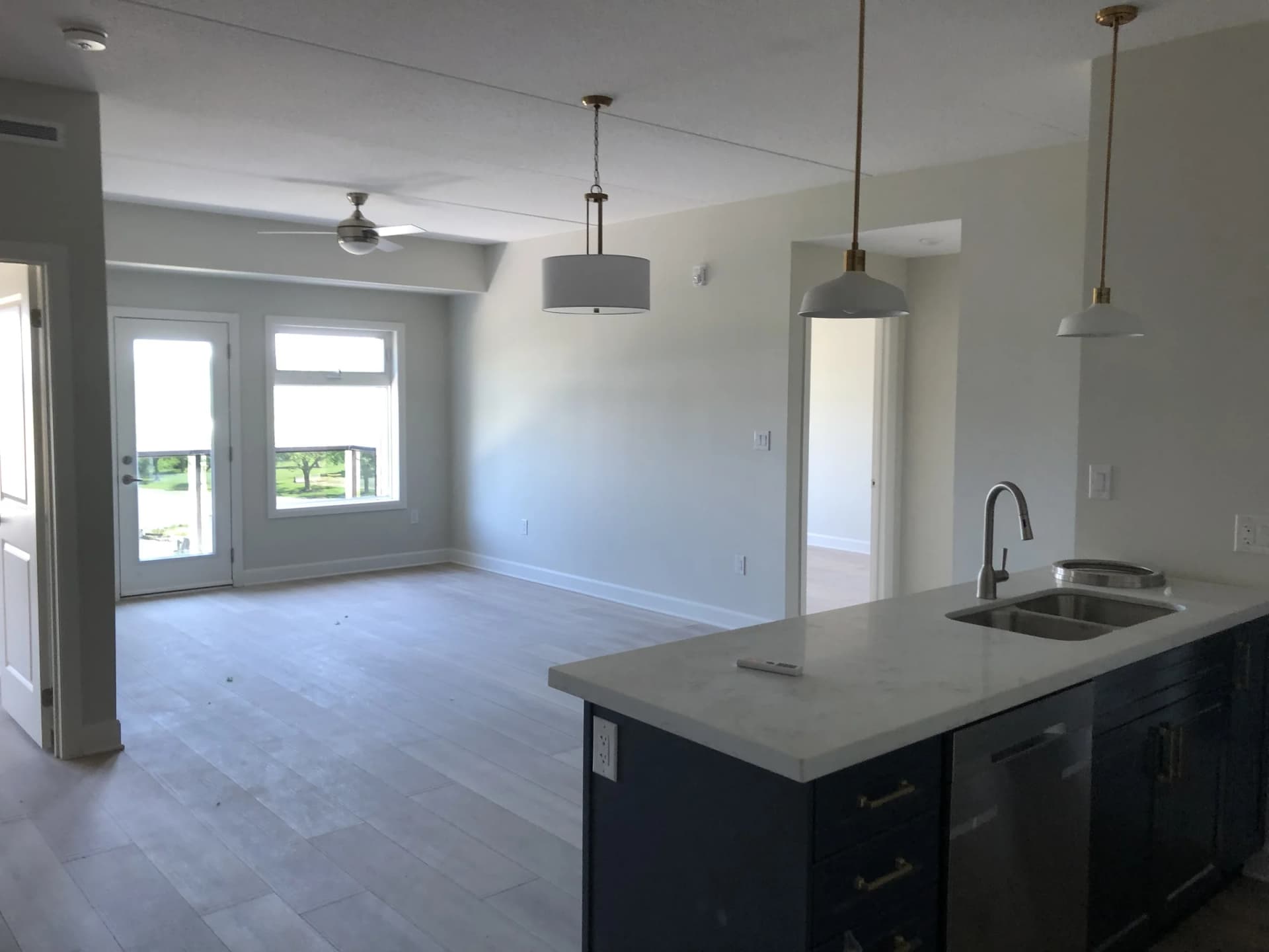 Open-plan apartment living and dining space beside a kitchen island, with pendant lighting and a glazed balcony door