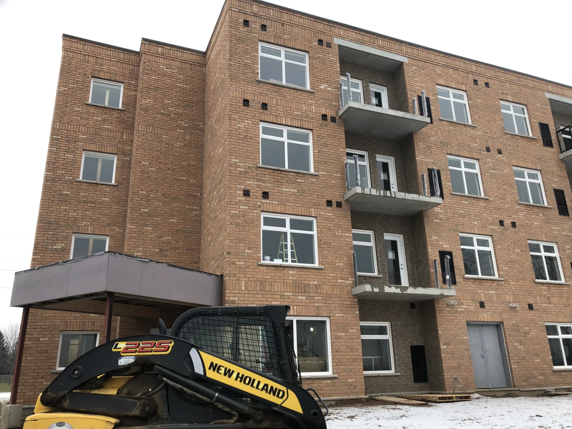 Supplied winter photograph of the entrance canopy and stacked balconies at 5629 Swayze Drive with a construction vehicle in the foreground